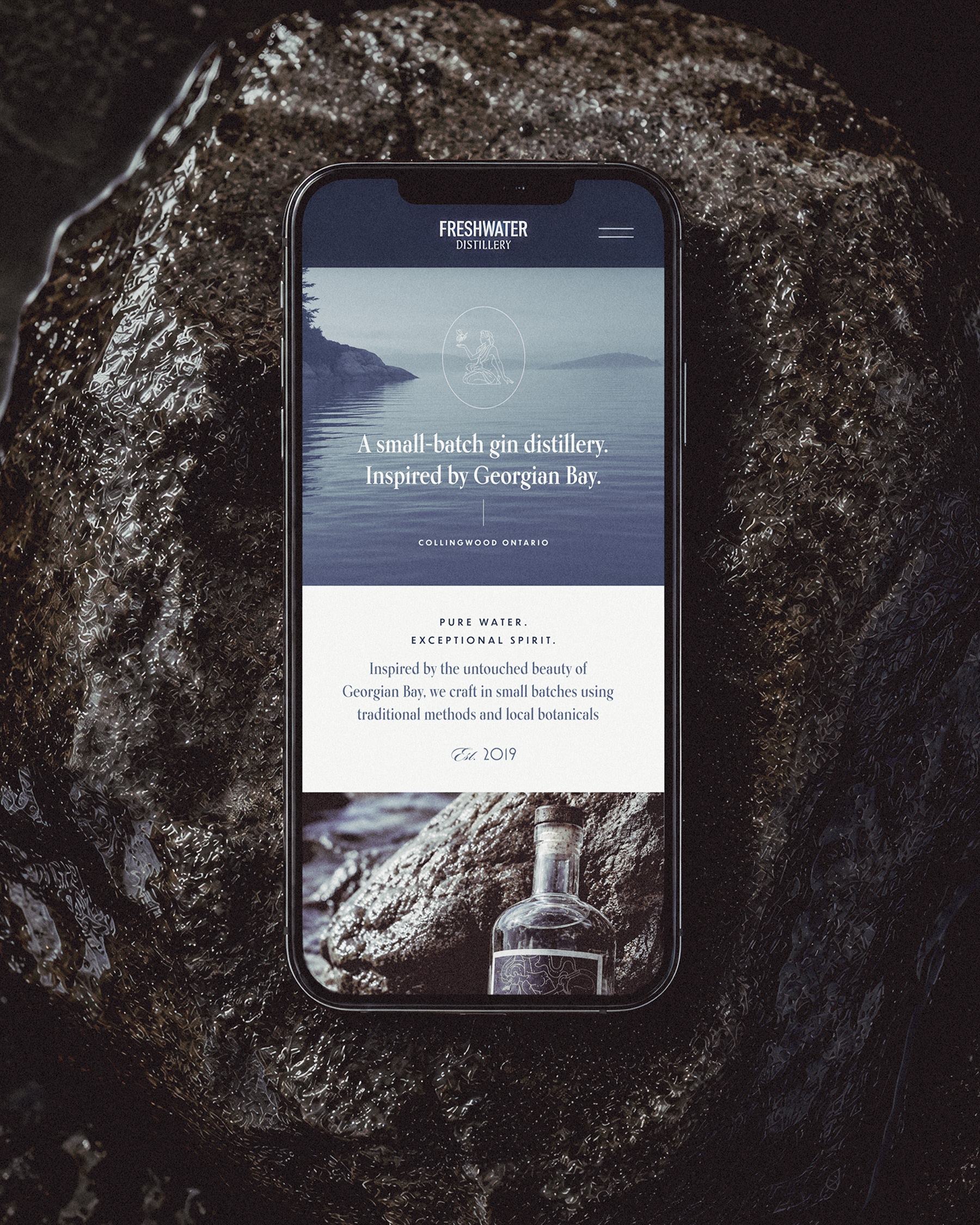 Freshwater Distillery mobile website displayed on a smartphone resting on a damp rock.