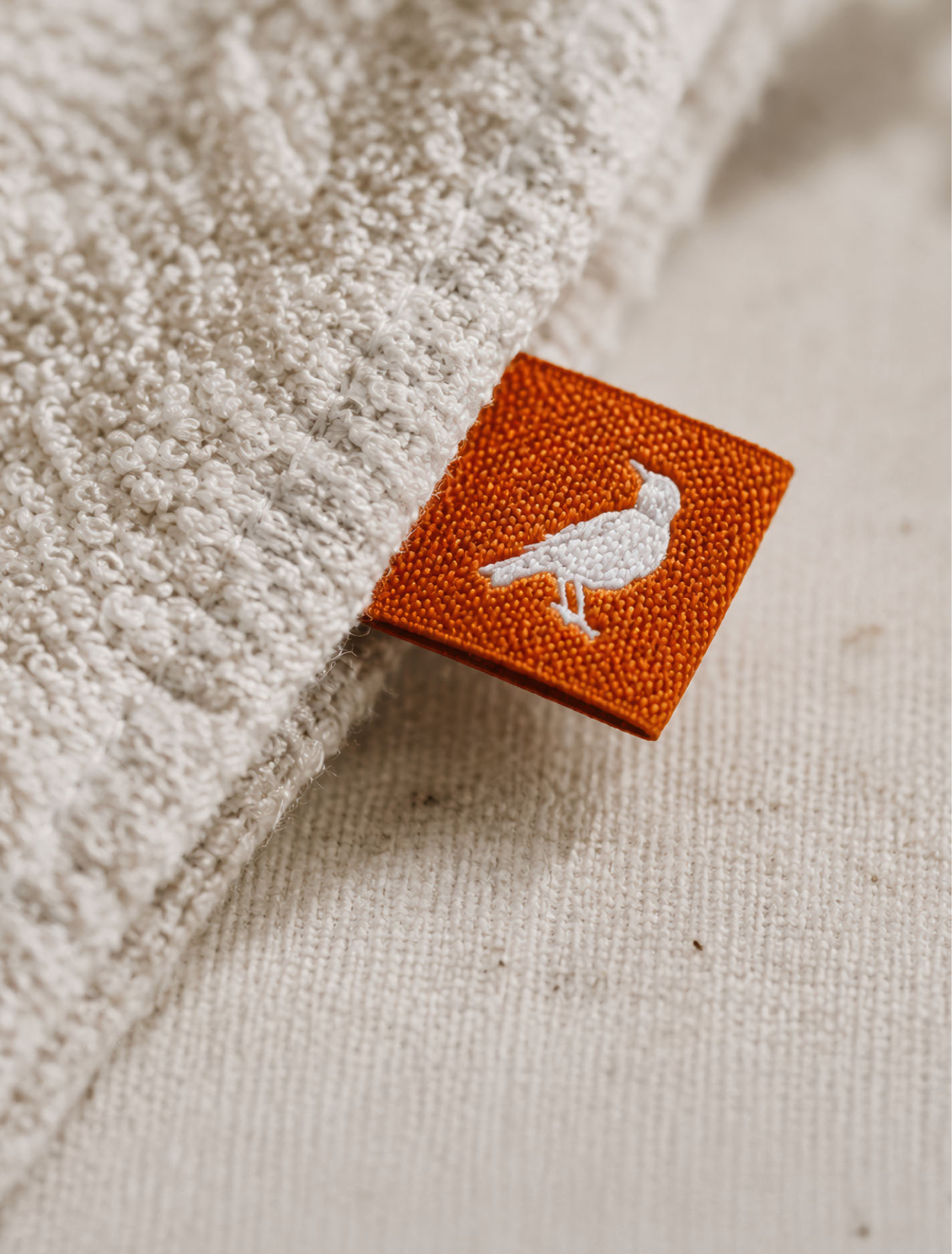 Orange Mike Fuhr fabric tag featuring a white robin symbol sewn onto textured fabric.